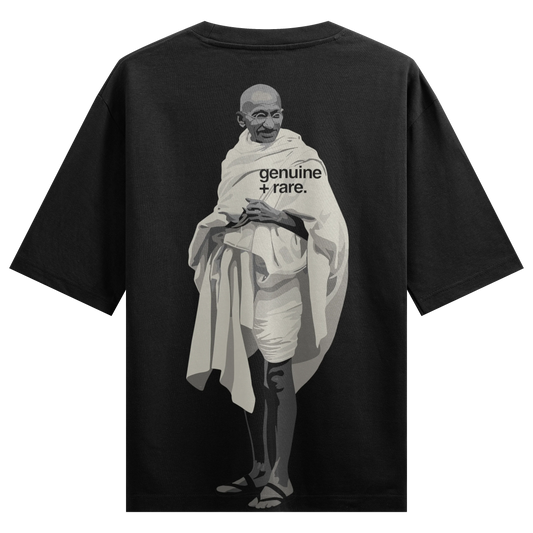 A monochromatic graphic illustration of Mahatma Gandhi on a black t-shirt featuring the text genuine + rare overlaid on hi...