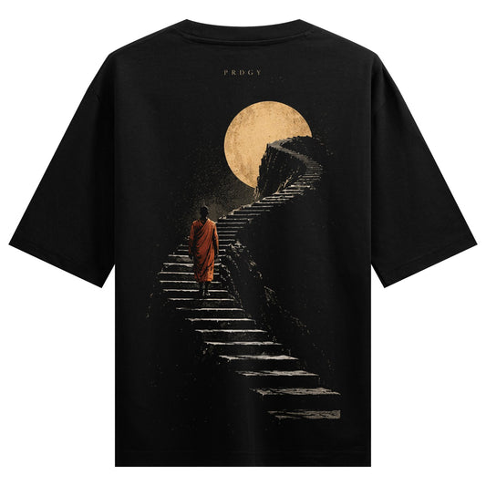 Ascension Path Oversized T-Shirt — a dark t-shirt features a monk in an orange robe walking up stone stairs towards a large