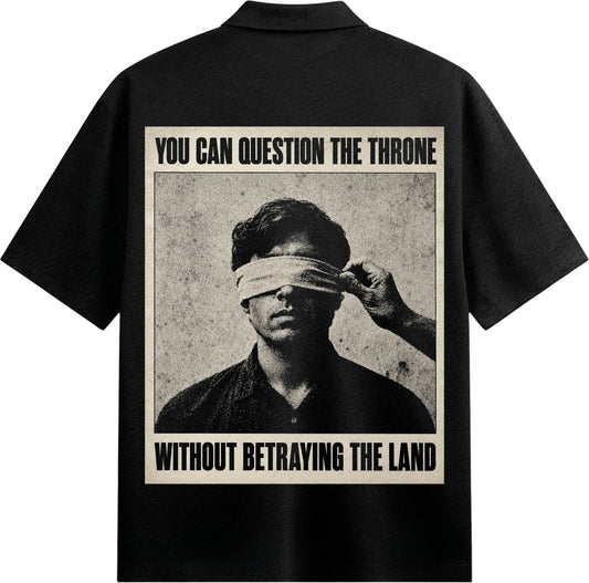 A black and white graphic on a black shirt shows a man blindfolded with a hand adjusting the blindfold set against a textu...