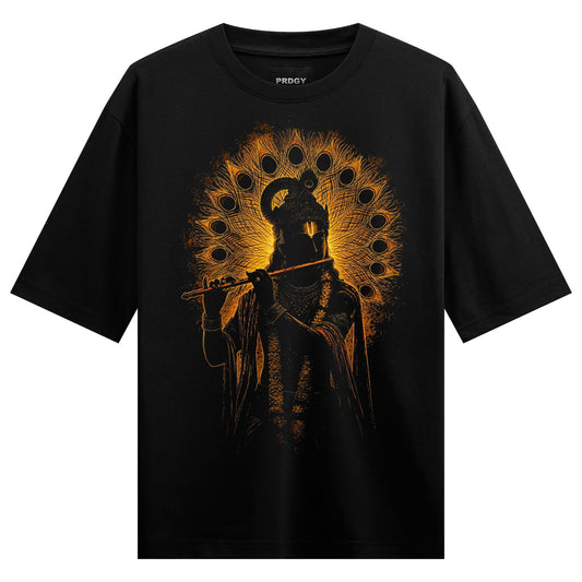 A black t-shirt features a golden-orange stylized depiction of Lord Krishna playing a flute surrounded by a radiant peacoc...