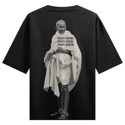 A grayscale portrait of Mahatma Gandhi is printed on the back of a black t-shirt with text overlaying his chest on PRDGY o...