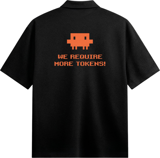 A black collared shirt with an orange pixelated alien graphic and pixelated text reading WE REQUIRE MORE TOKENS on the bac...